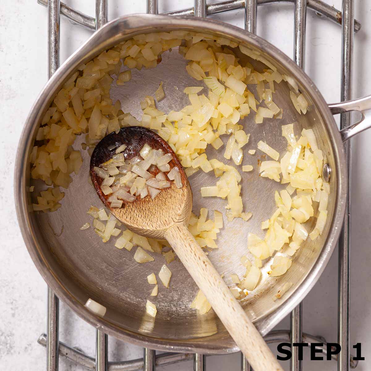 Cooked diced onion in a saucepan with a wooden spoon.