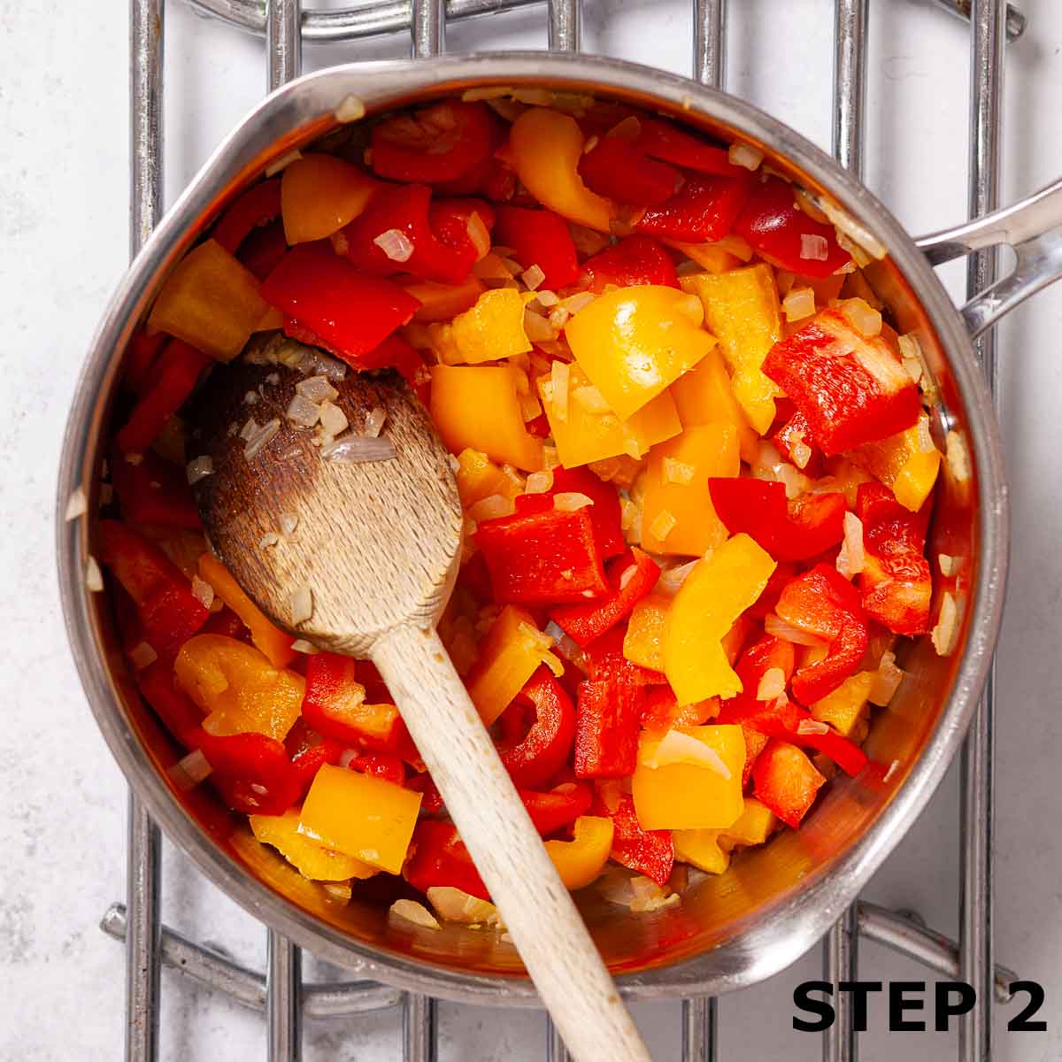 Chunks of red pepper and yellow pepper with diced onion in a saucepan.