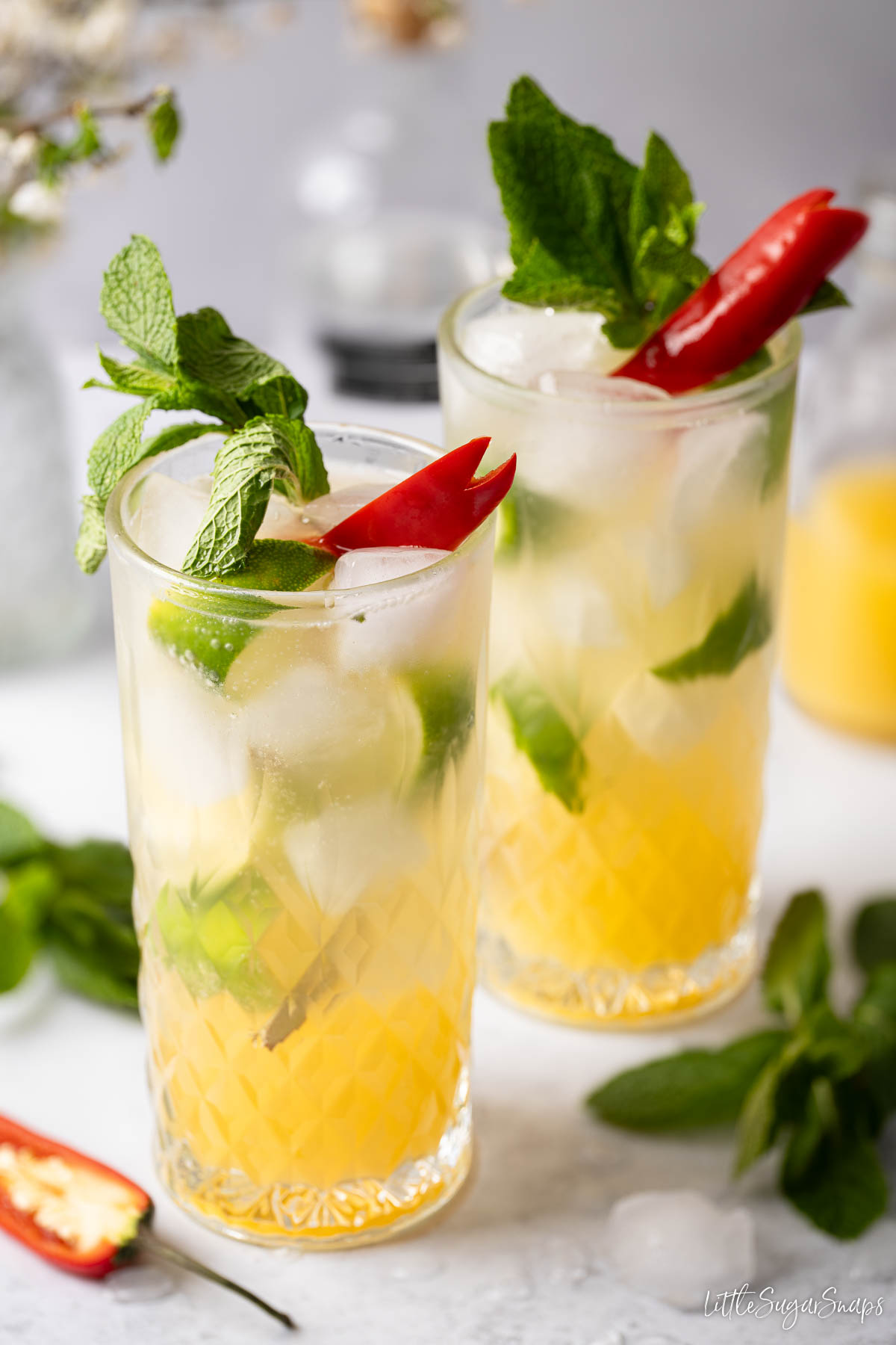 Mango and vodka cocktails served in highball glasses with mint, lime and chilli garnish.
