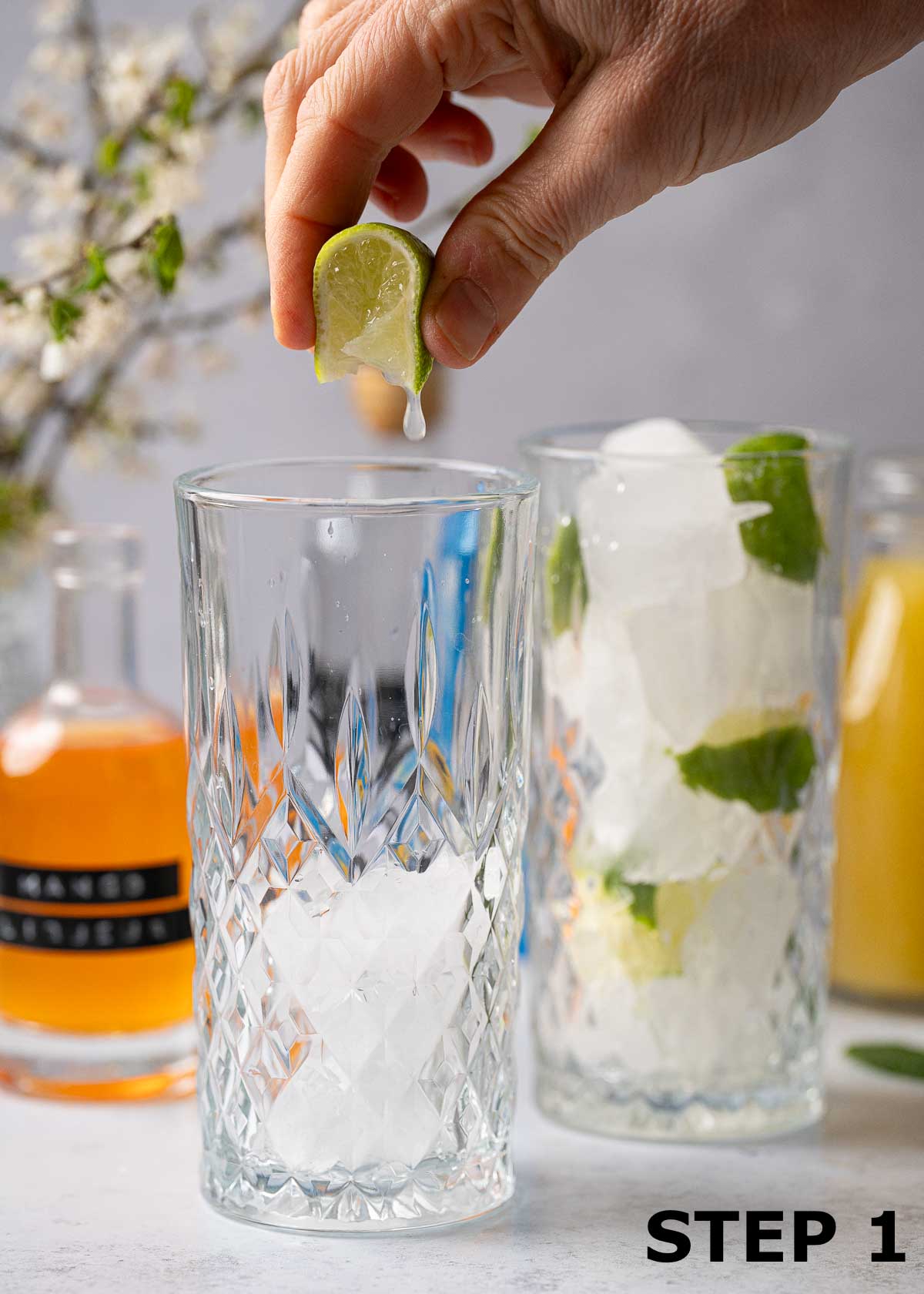 A wedge of lime being squeezed over a highball glass with ice in it.