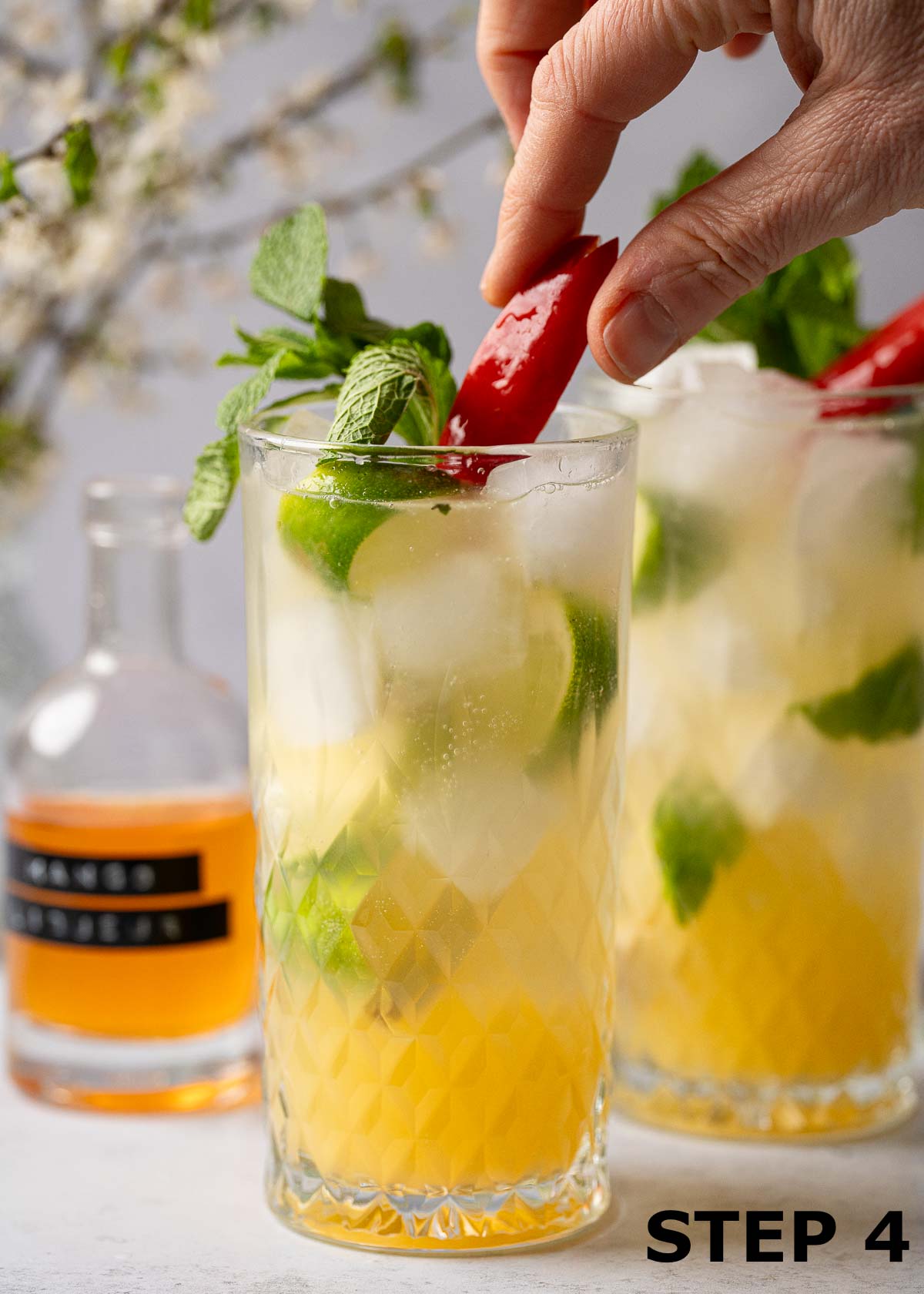 A person adding red chilli garnish to a vodka mango vocktail.