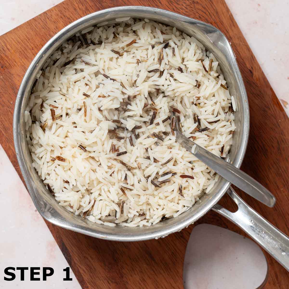 Cooked wild rice in a saucepan with a spoon in it.