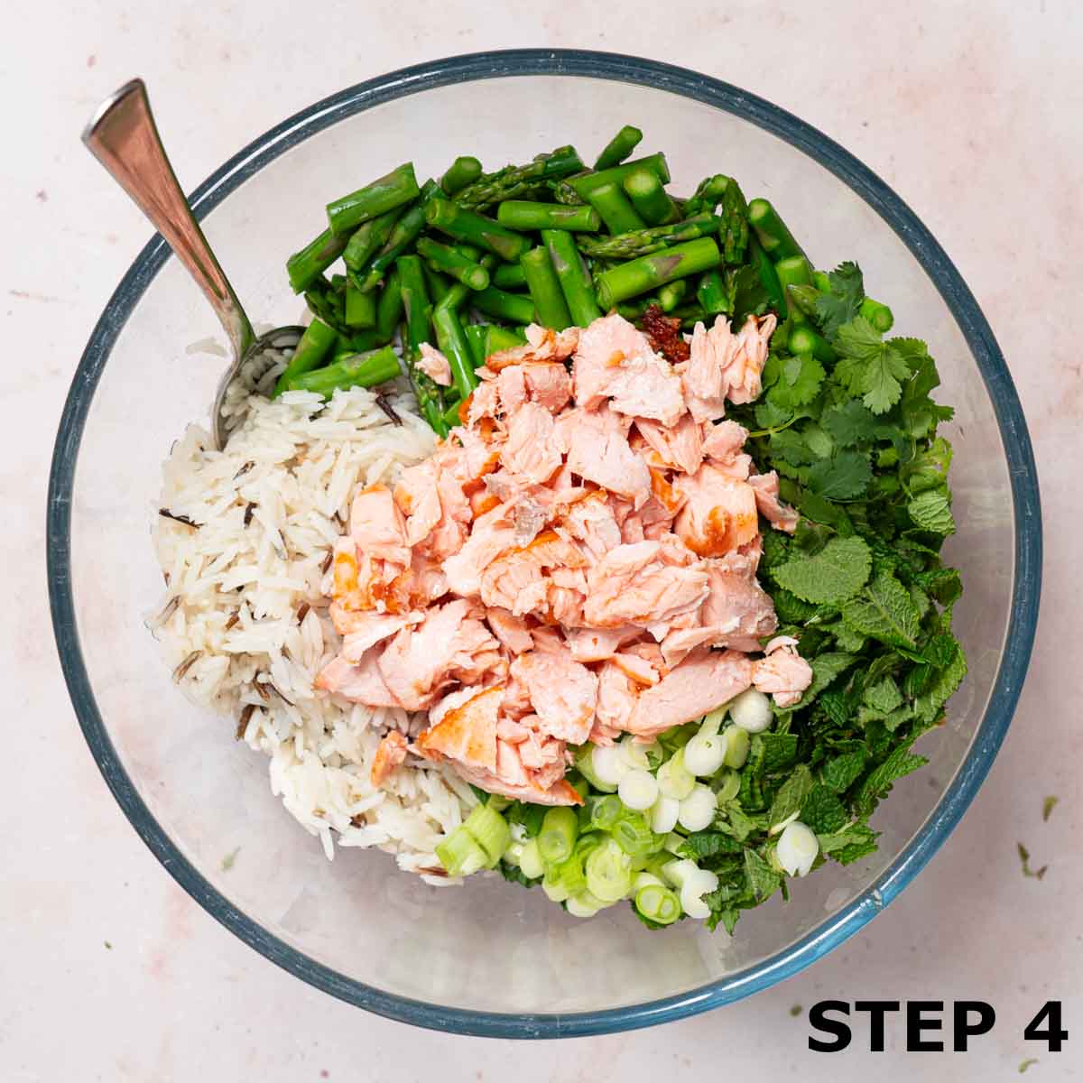 A bowl containing wild rice, flaked salmon, asparagus, mint, coriander and spring onions.