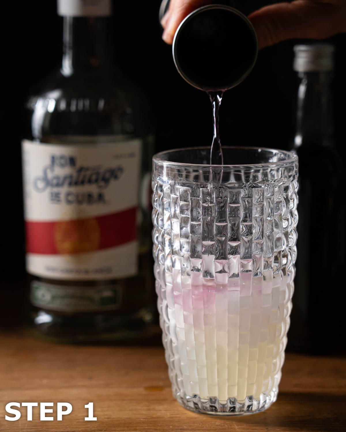 Violet syrup being poured into a cocktail shaker with ice and other daiquiri ingredients.