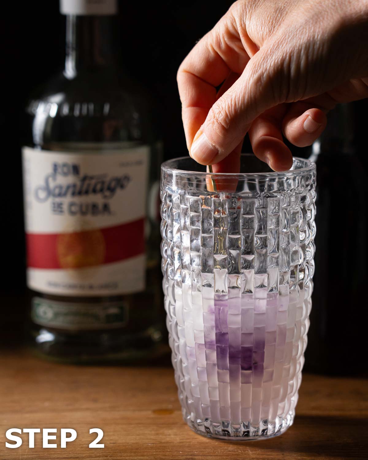 A person adding purple food colour to a daiquiri cocktail in a shaker.