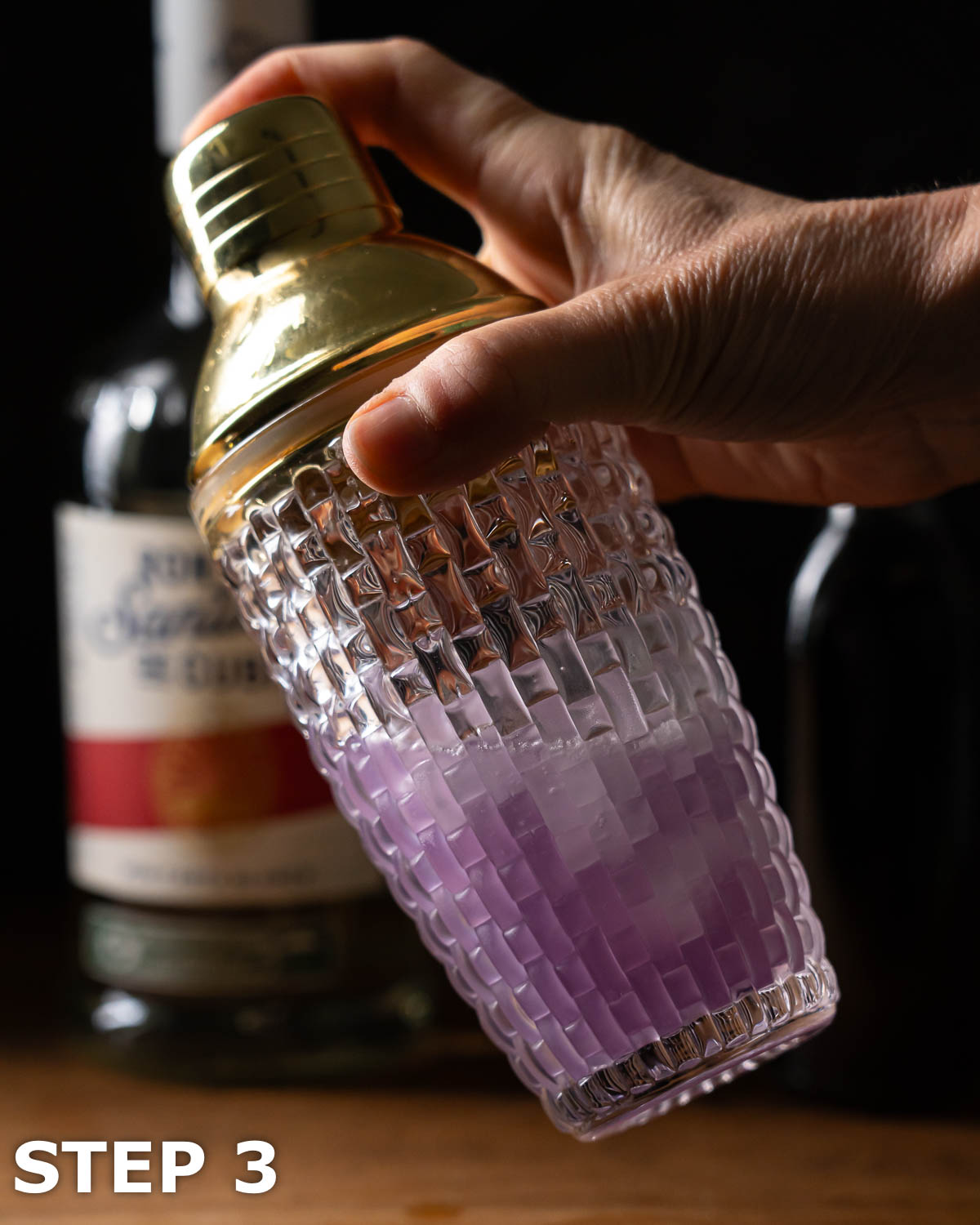 A person shaking a violet syrup cocktail with ice.