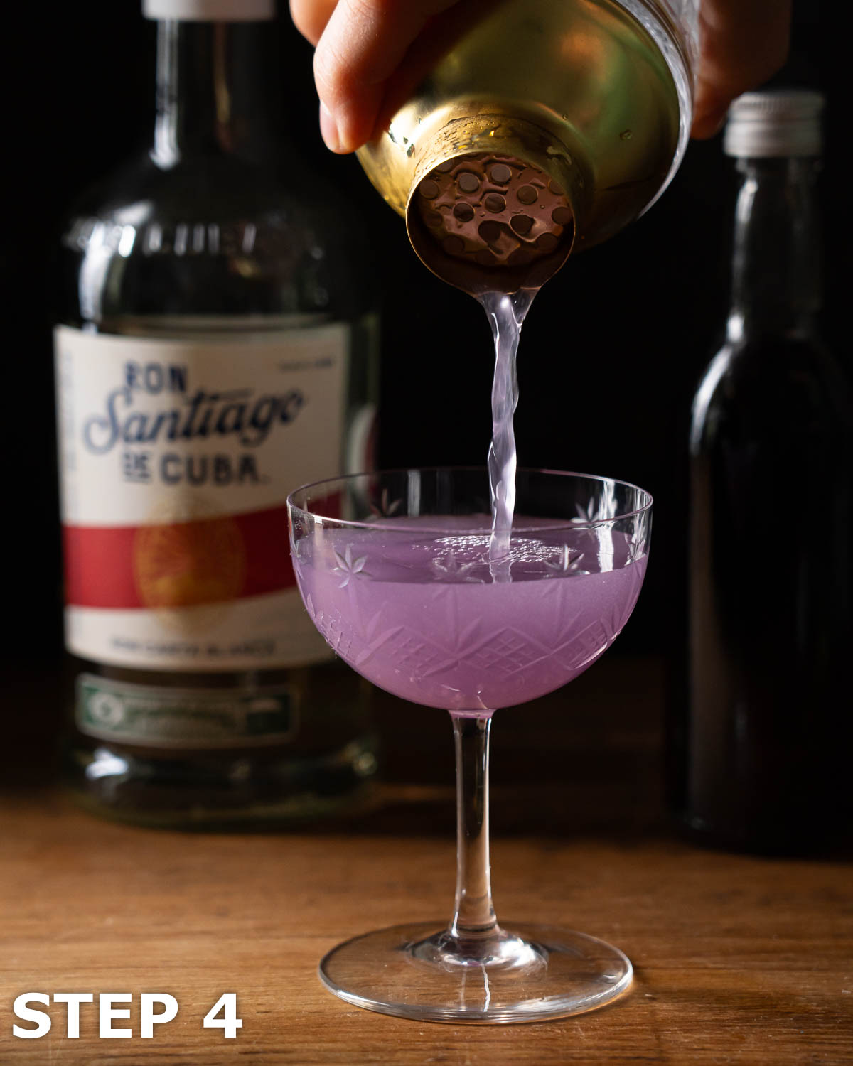 A person straining a violet cocktail into a vintage cocktail glass.