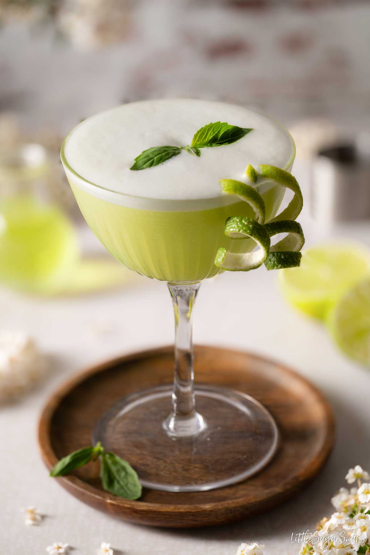 A basil cocktail with egg white foam, basil leaf and lime zest garnishes.