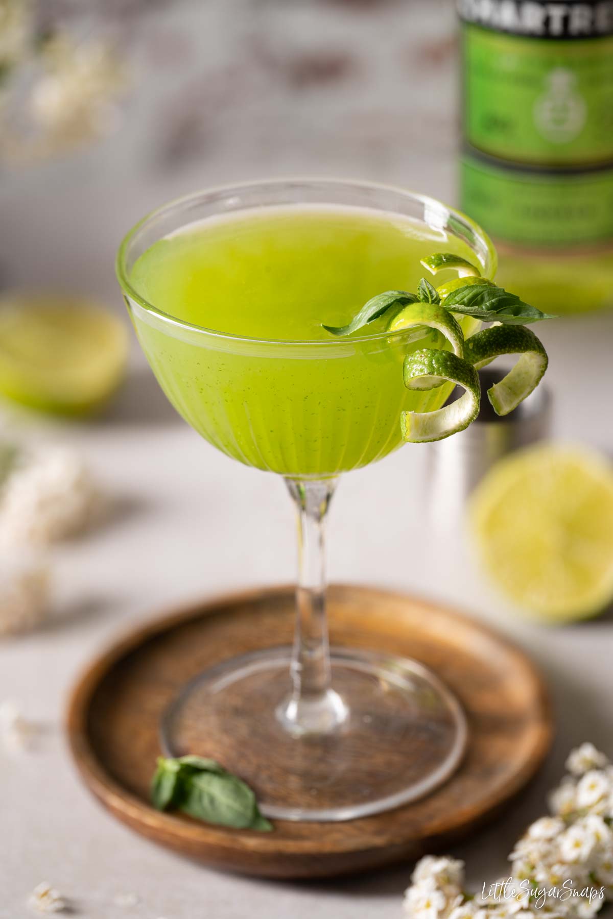 A basil gin cocktail with spirals of lime zest and basil leaf garnish.