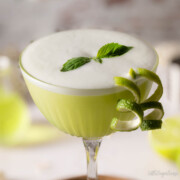 A basil cocktail with egg white foam, basil leaf and lime zest garnishes.