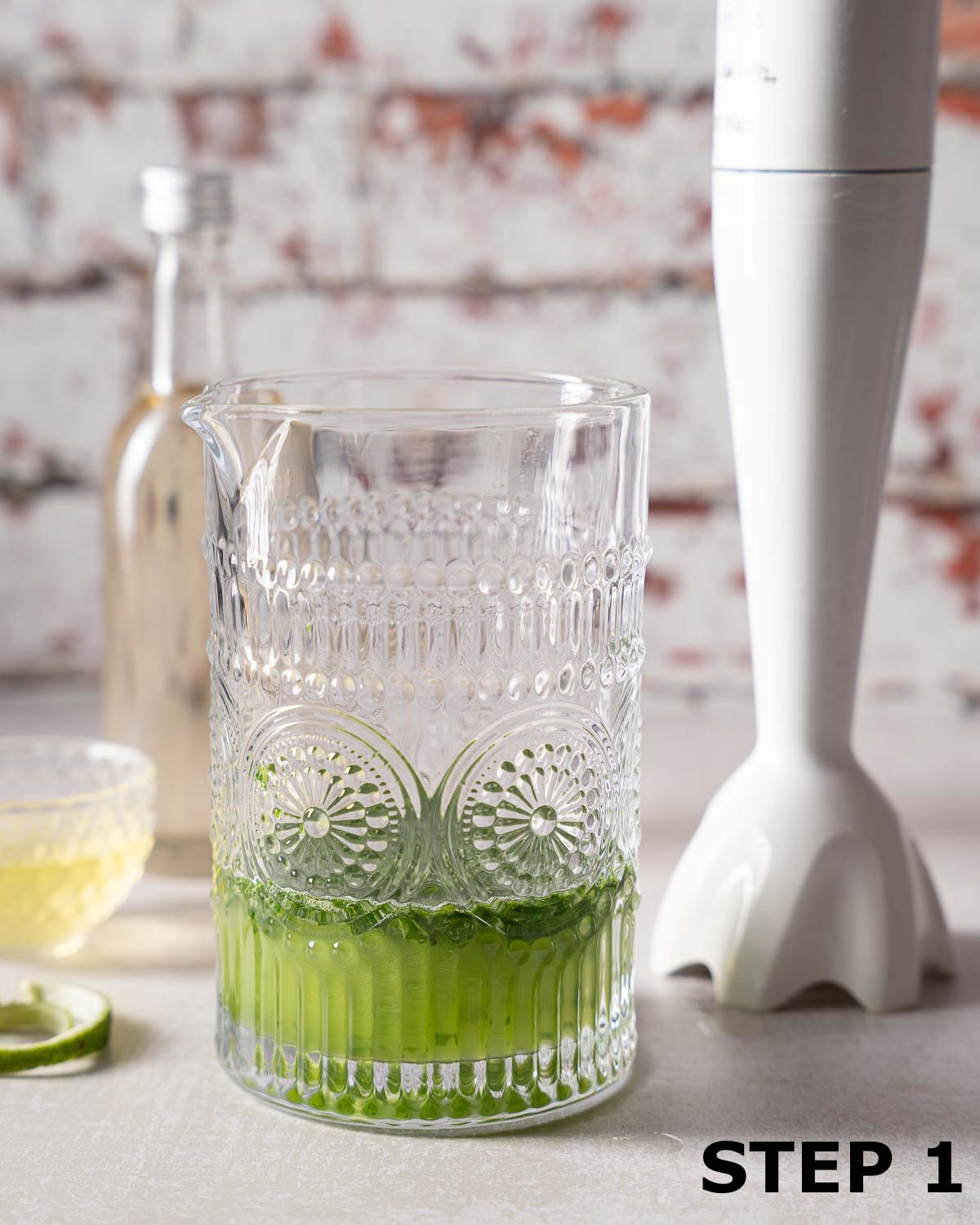 Gin and basil in a cocktail jug with a stick blender at the side.