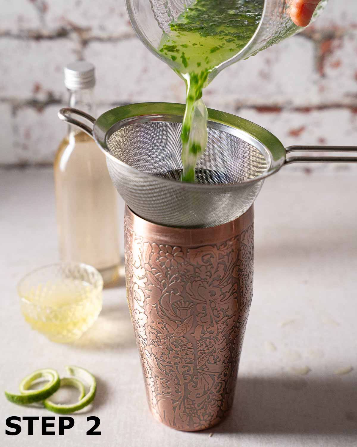 Gin and basil being strained through a sieve into a cocktail shaker.