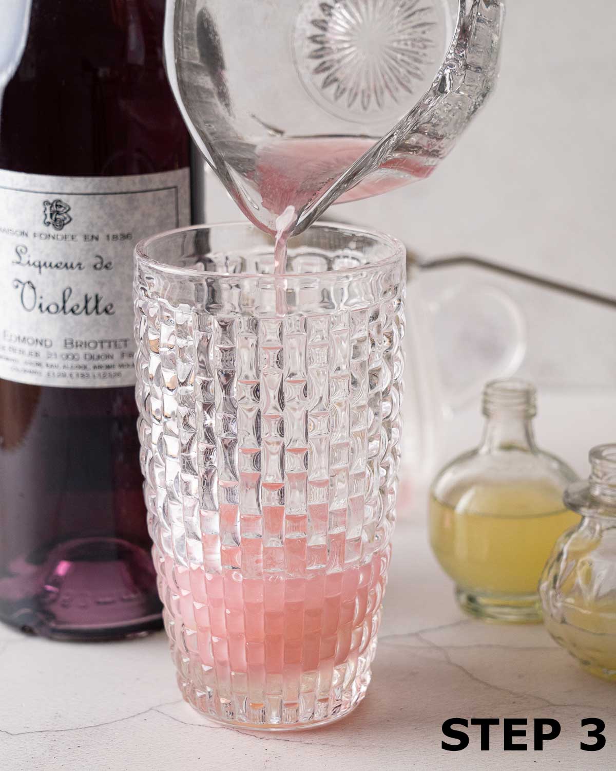 Blueberry gin being poured into a glass cocktail shaker.