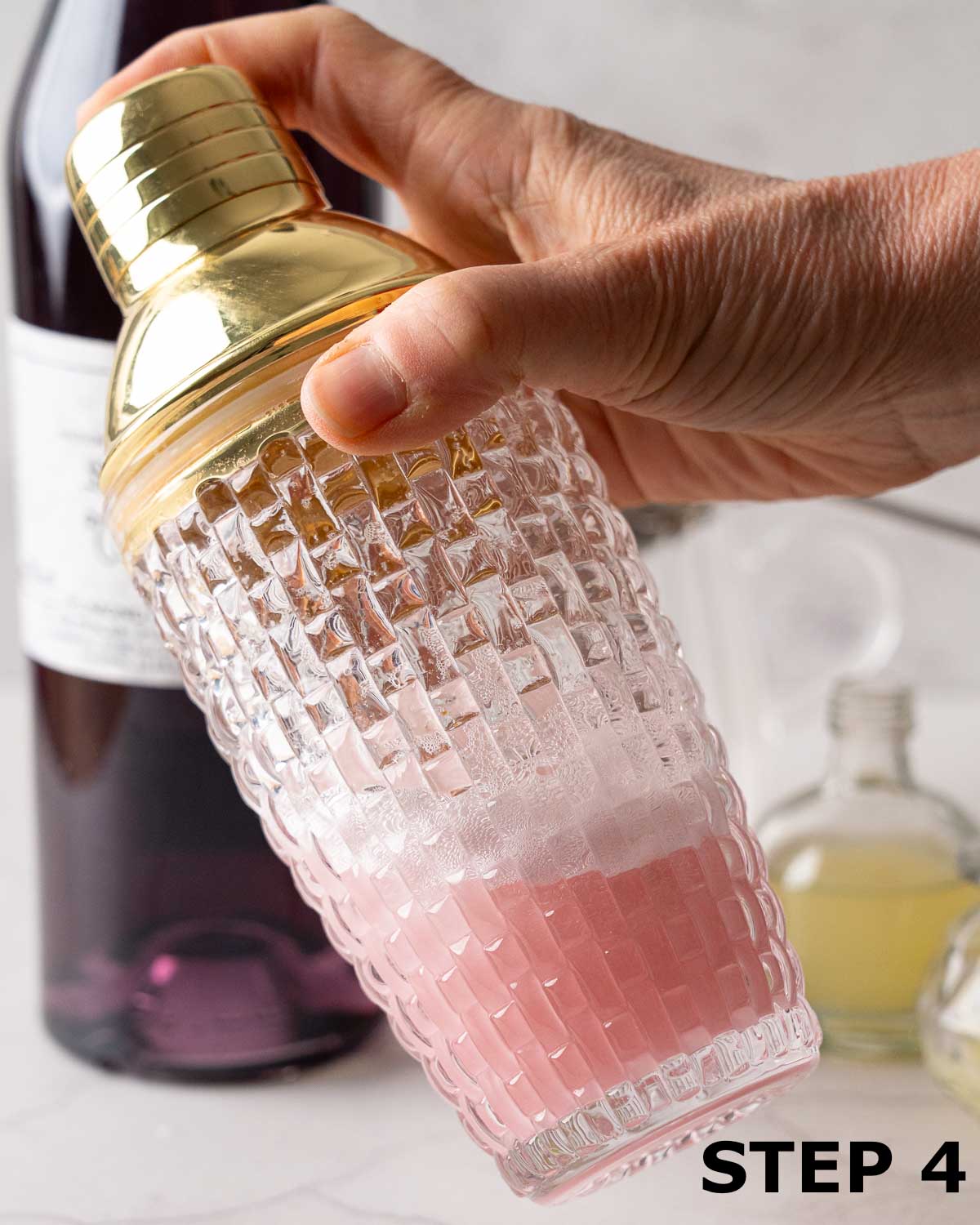 A person shaking a blueberry gin cocktail in a shaker.