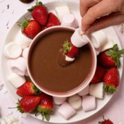 A person dipping skewered marshmallows and strawberries into chocolate dip.