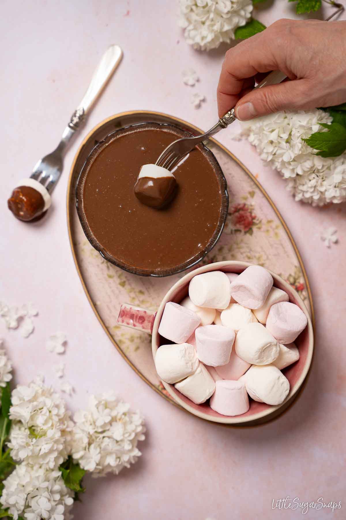 A marshmallow on a fork being dipped into chocolate dipping sauce with a bowl of marshmallows alongside.