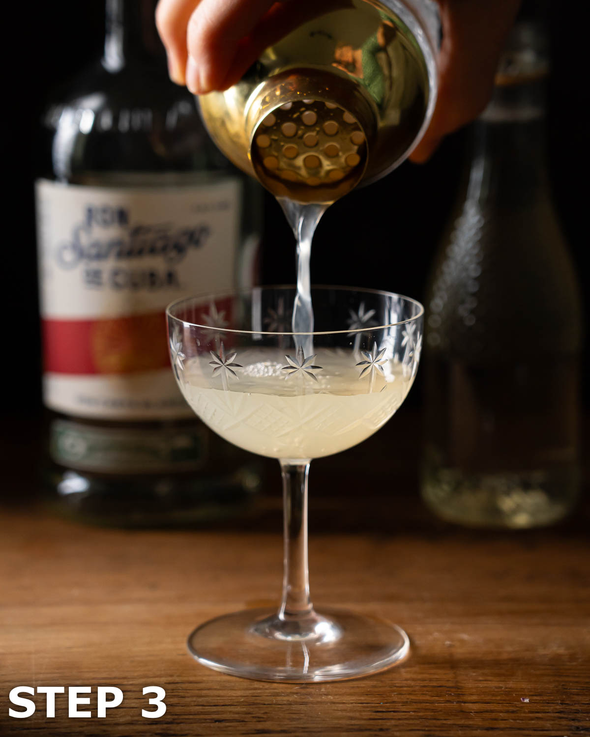 A person pouring a white rum and lime cocktail into a coupe glass.