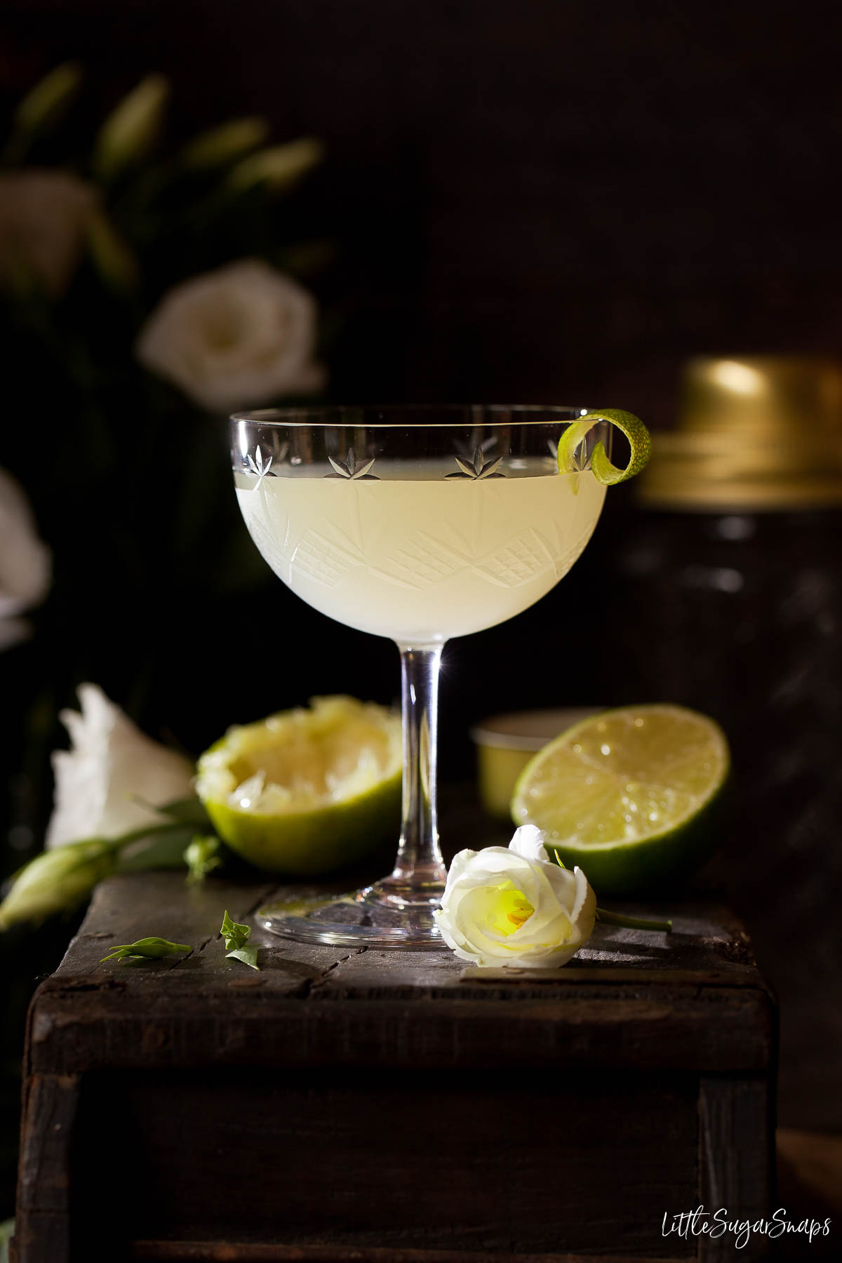 A classic daiquiri cocktail with lime zest garnish in a dark setting.
