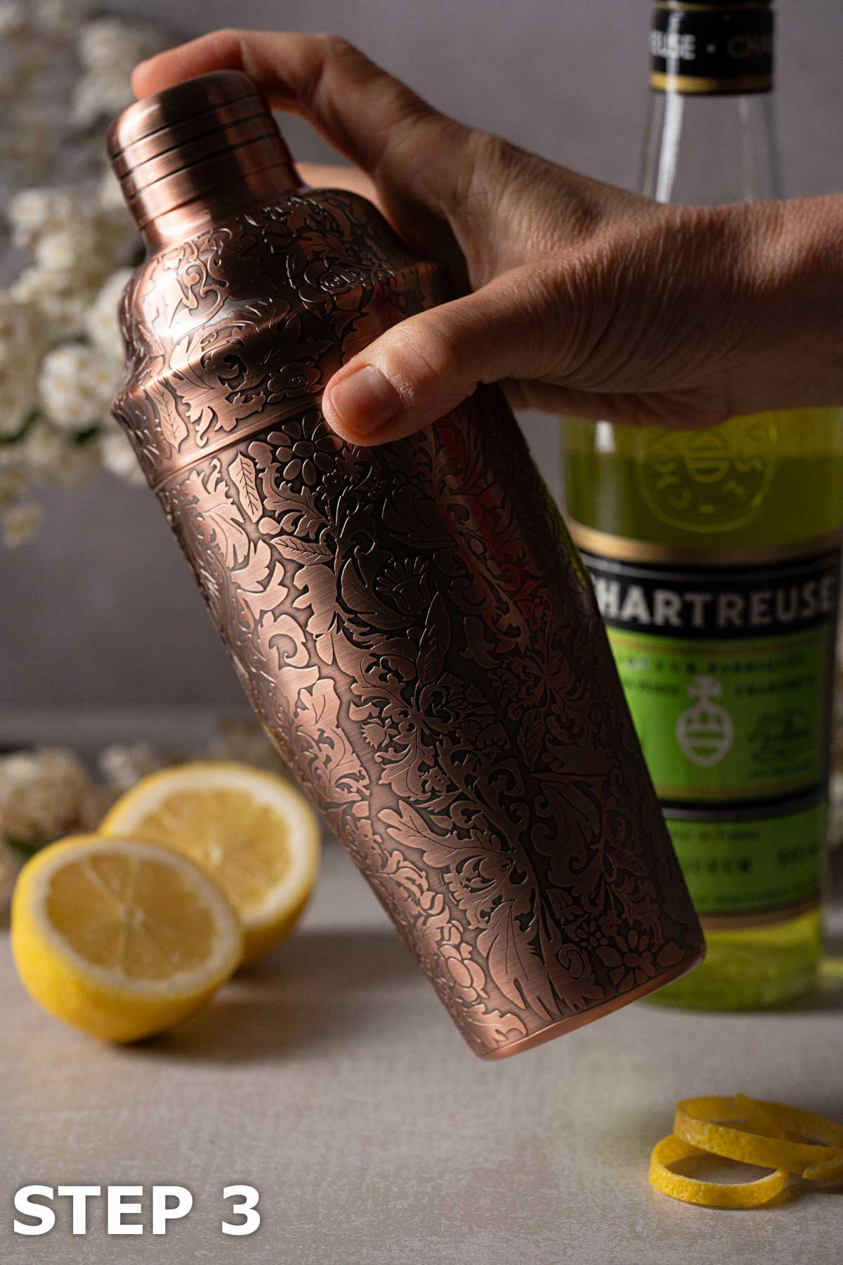 A person shaking a copper embossed cocktail shaker.