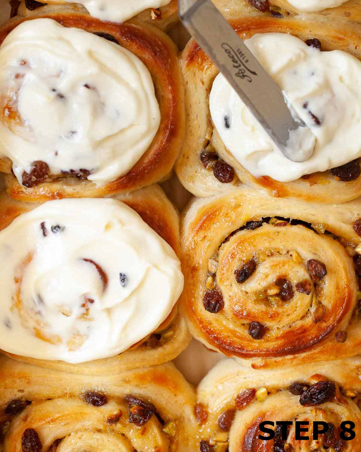 Baked lemon rolls with cream cheese frosting being spread on the top.