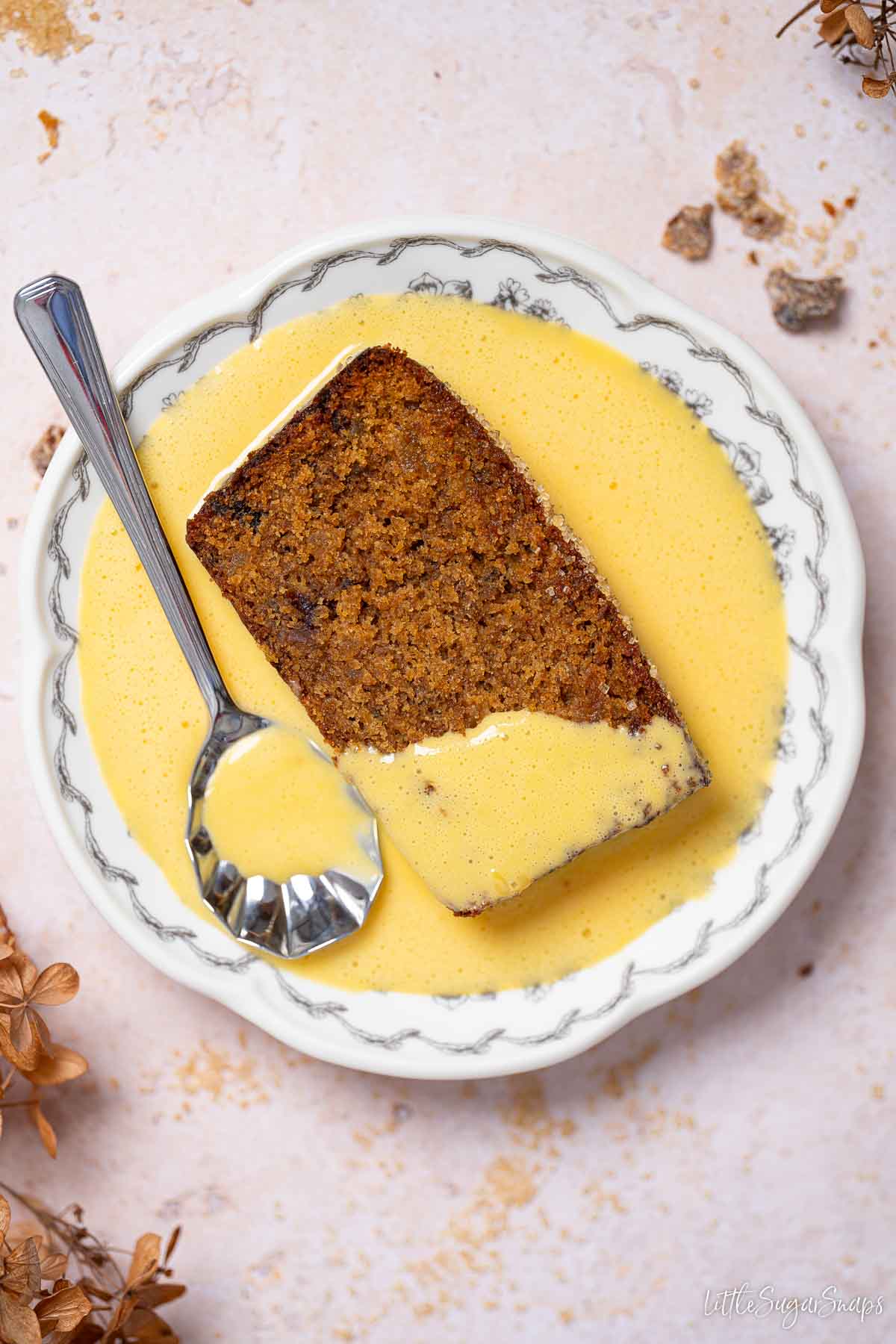 A slice of moist date cake and custard on a plate with a vintage spoon.