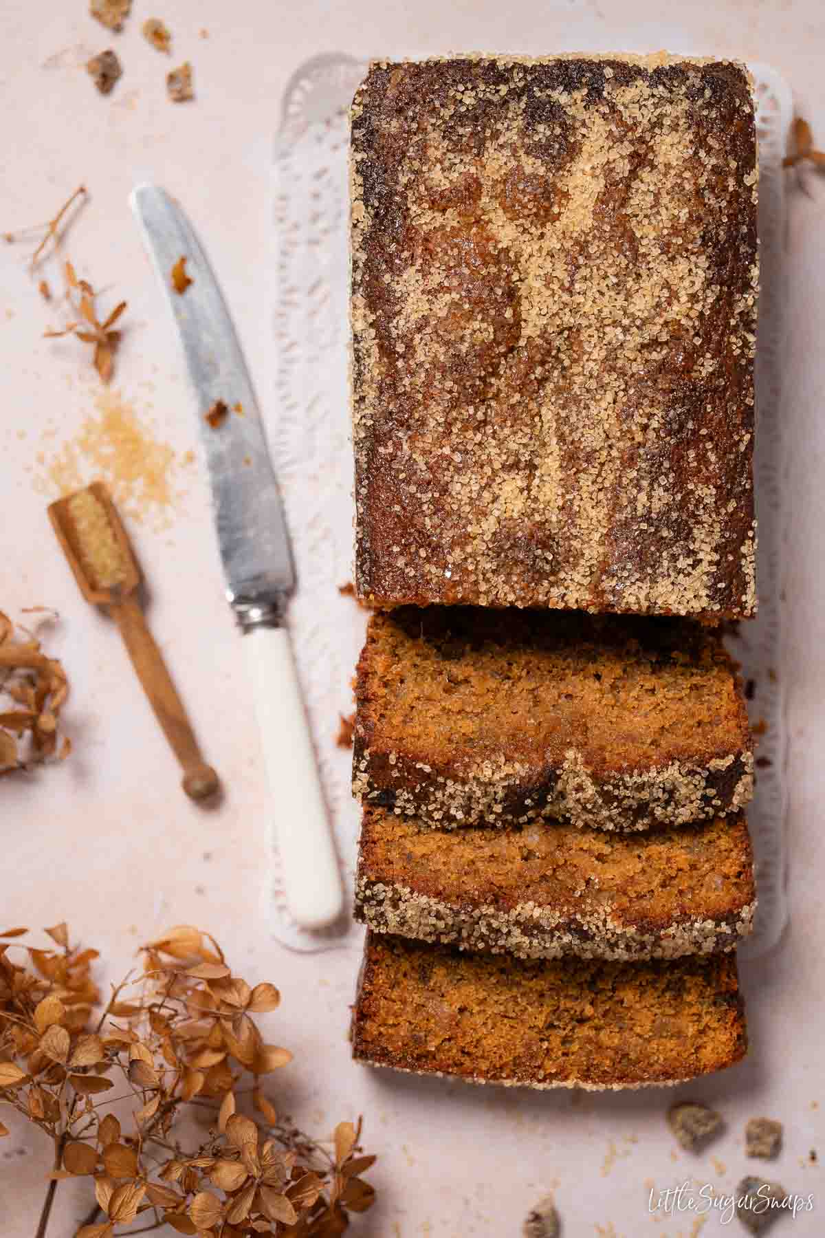 Sticky date loaf cake with crunchy Demerara sugar topping with three slices cut from it.