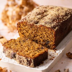 A sticky date cake with a slice cut and lying in front of the cake.