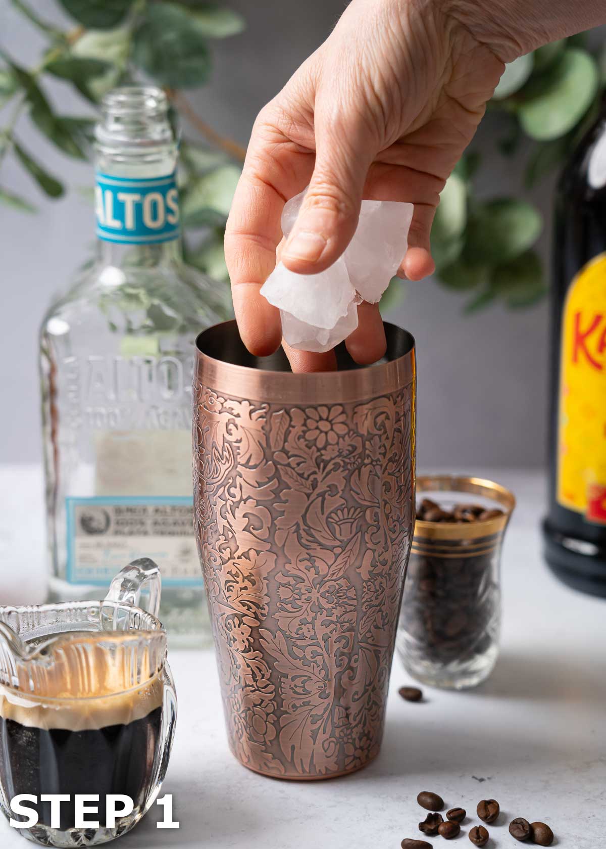 A person adding ice cubes to the base of a copper cocktail shaker.