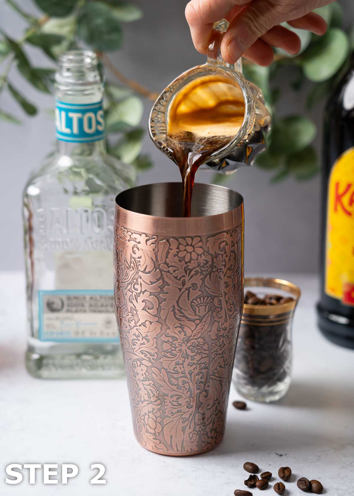A person pouring hot espresso into a copper cocktail shaker.