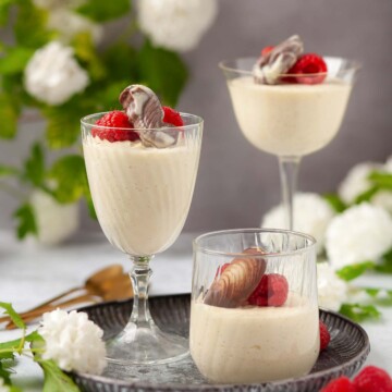 Three glasses of white chocolate mousse with chocolate and raspberry garnish.