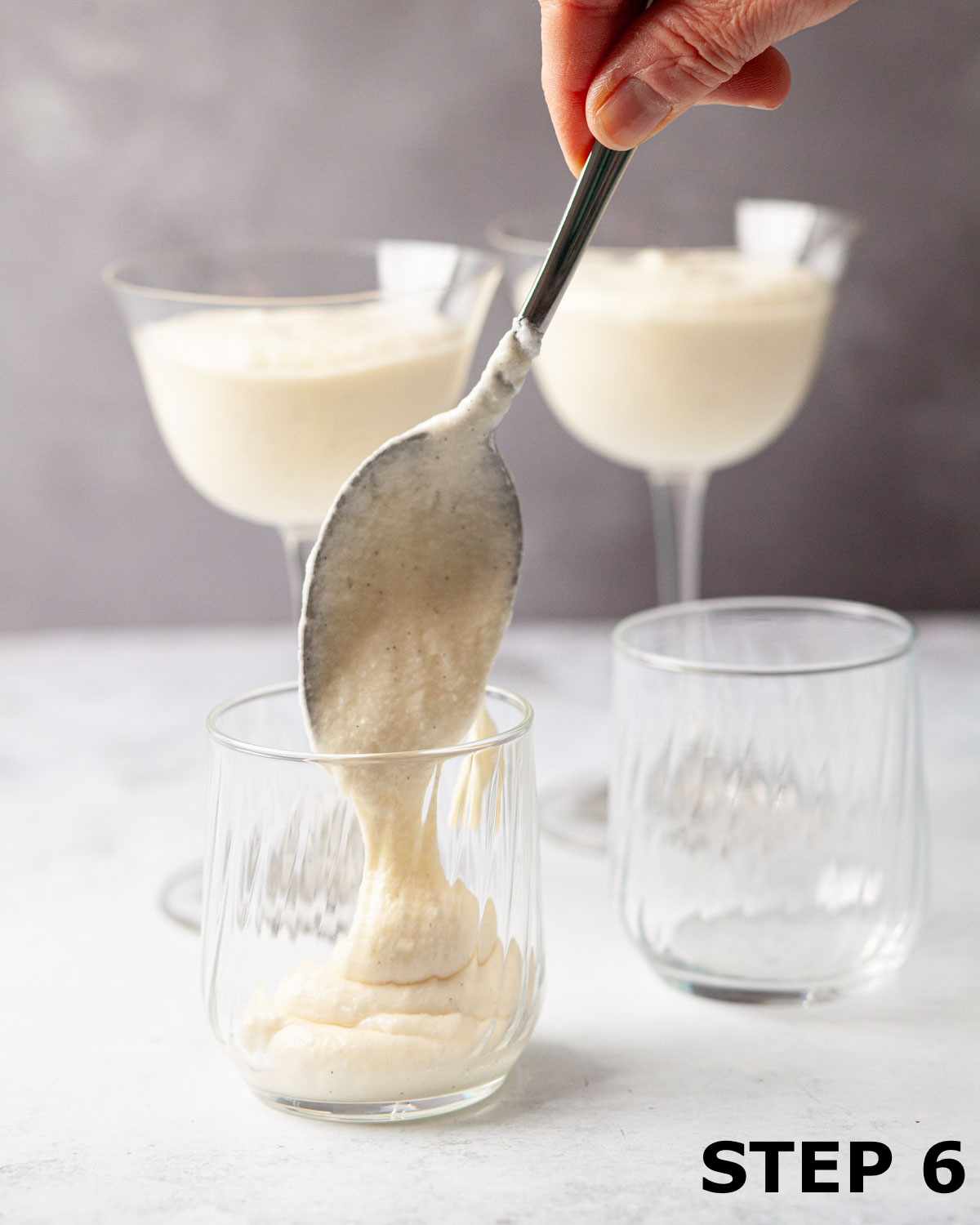 A person spooning white chocolate mousse into glasses.