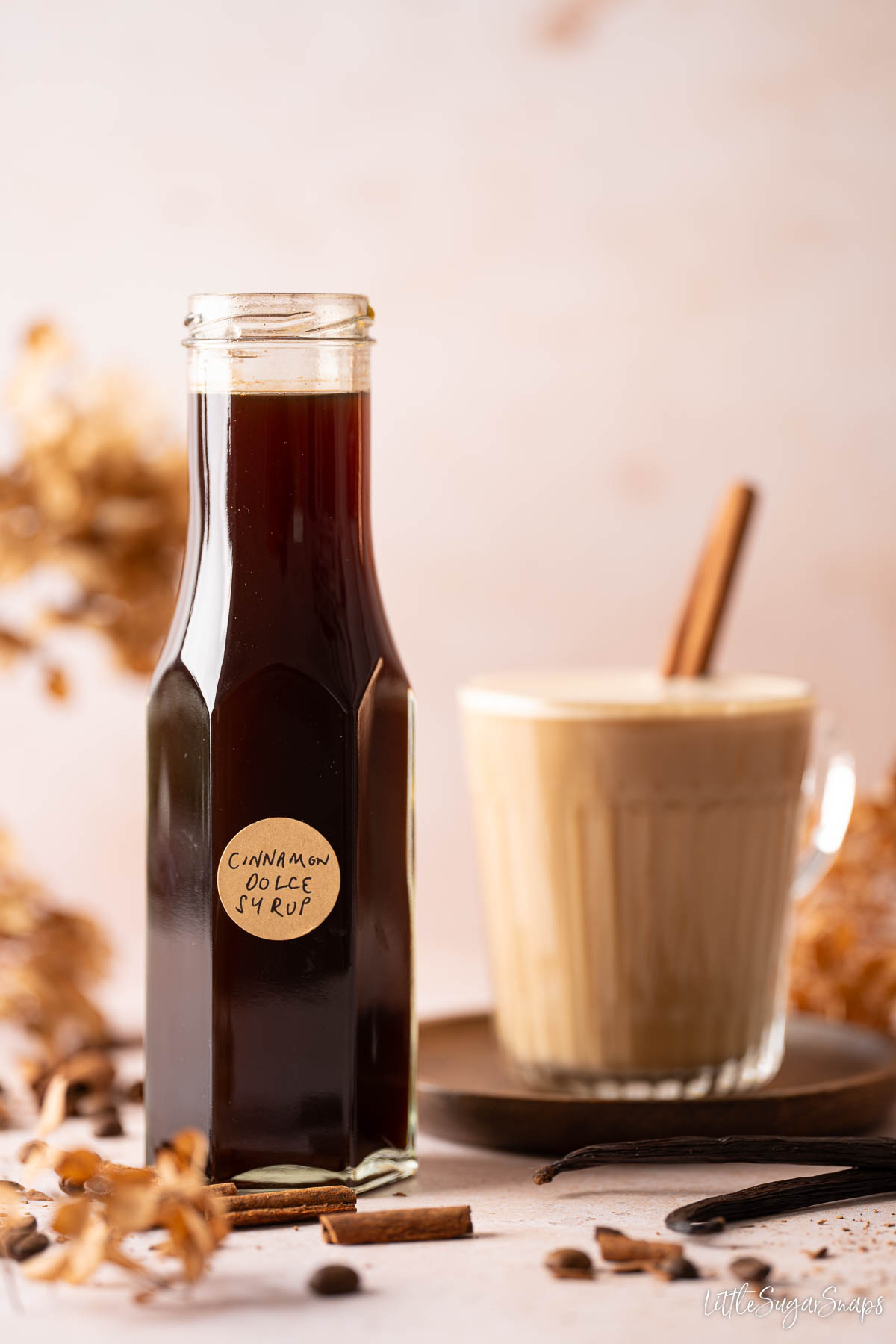A bottle of cinnamon dolce syrup with a cinnamon latte behind it.