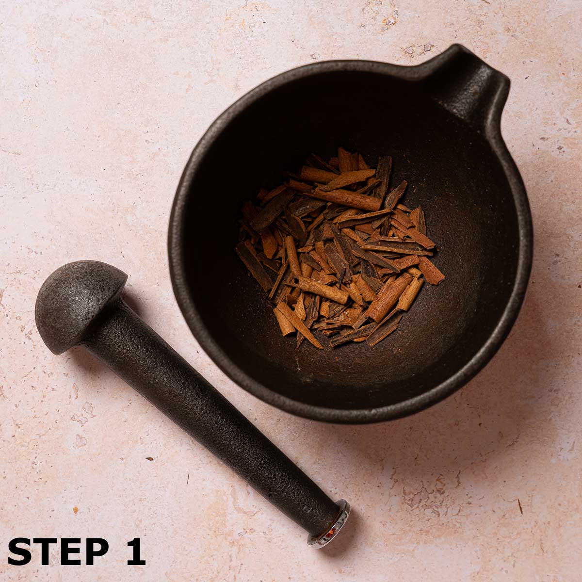 Roughly crushed cinnamon sticks in a mortar bowl with pestle alongside.