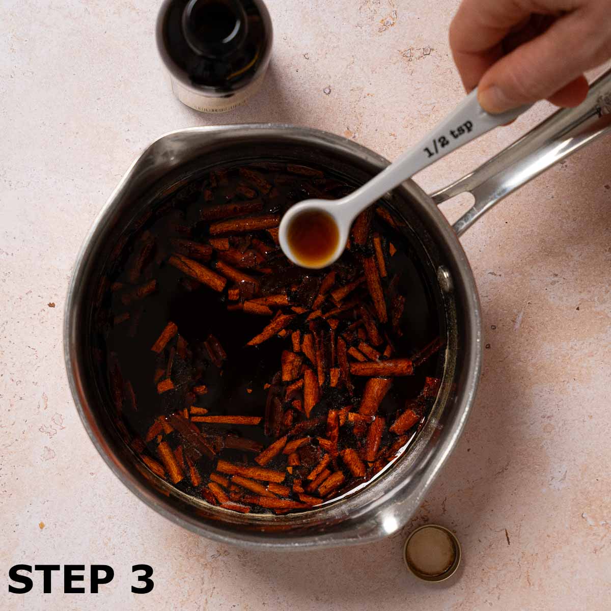 A person adding vanilla extract to a pan of cinnamon syrup.