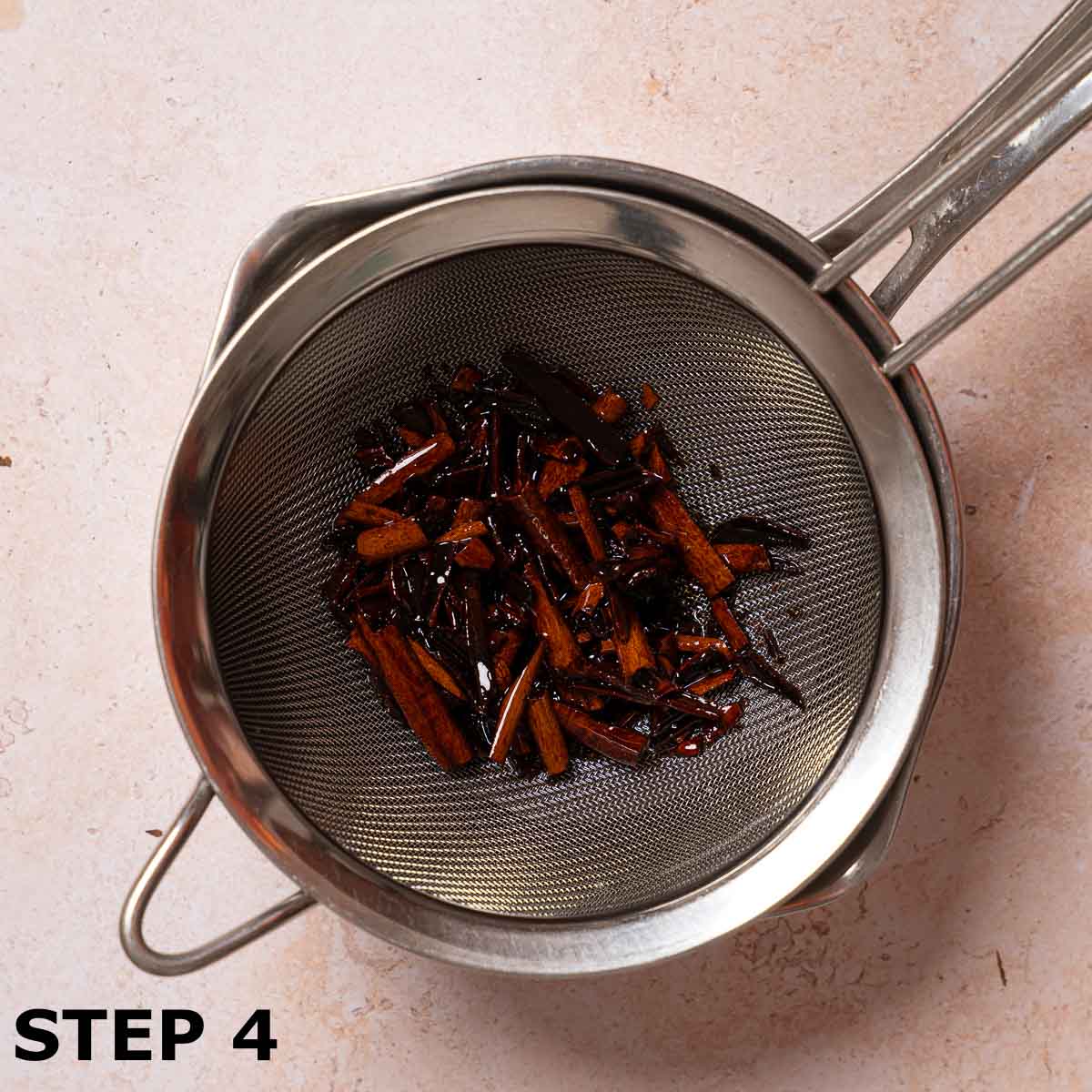 Drained crushed cinnamon in a sieve suspended over a pan to collect the syrup.