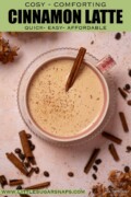 Latte with cinnamon garnishes in a pink coffee cup with text overlay.