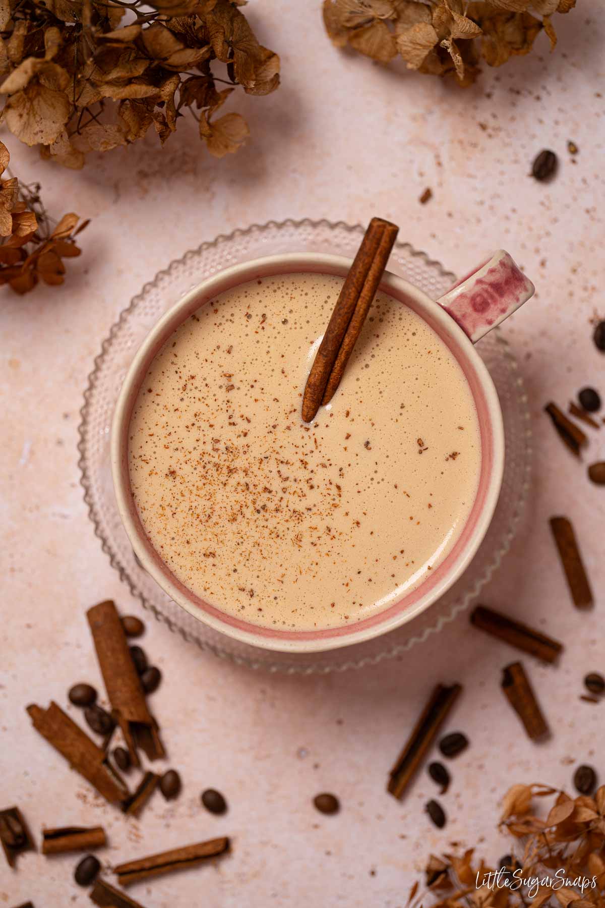 Latte with cinnamon garnishes in a pink coffee cup with broken cinnamon on the worktop.