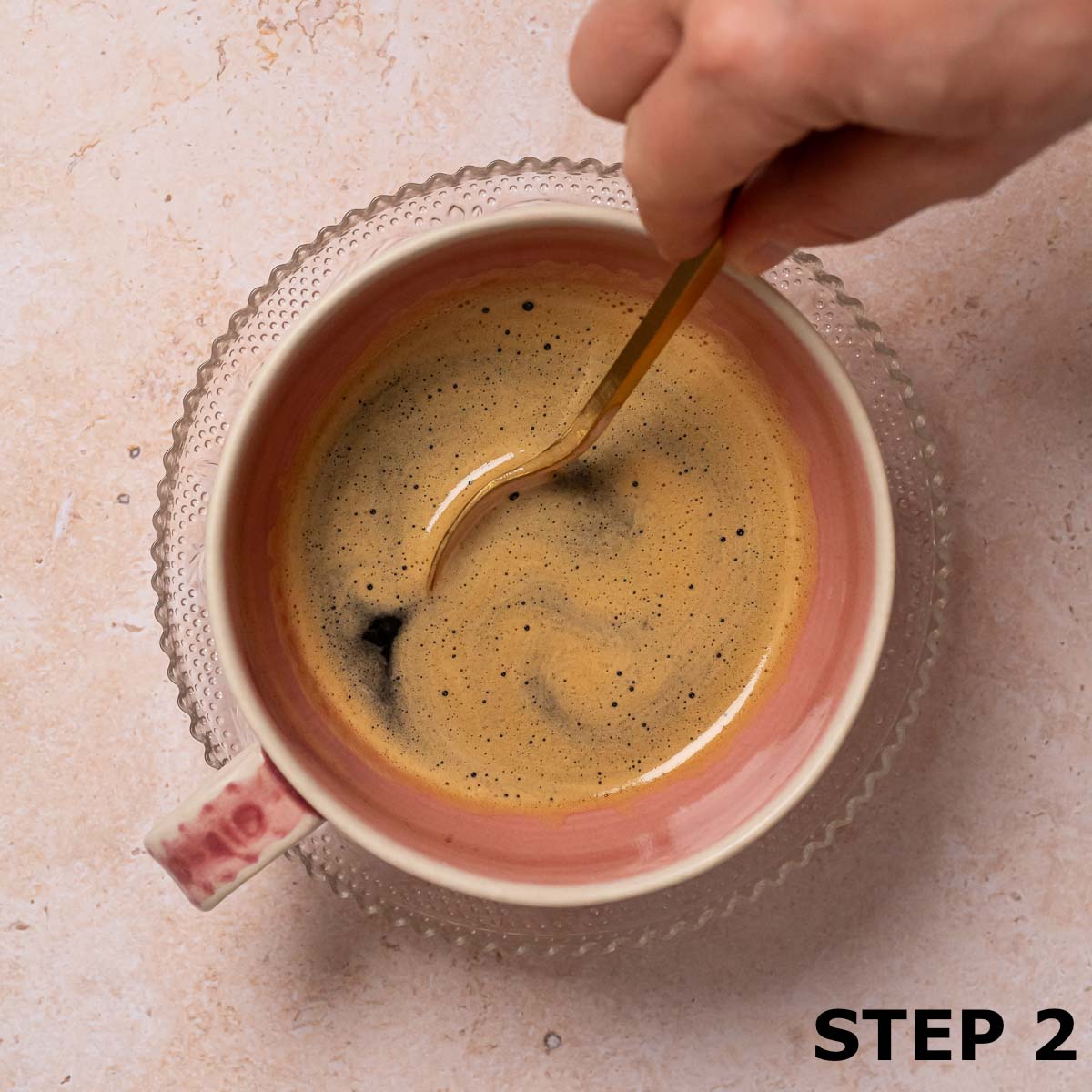 A person stirring coffee in a pink coffee cup with a gold teaspoon.