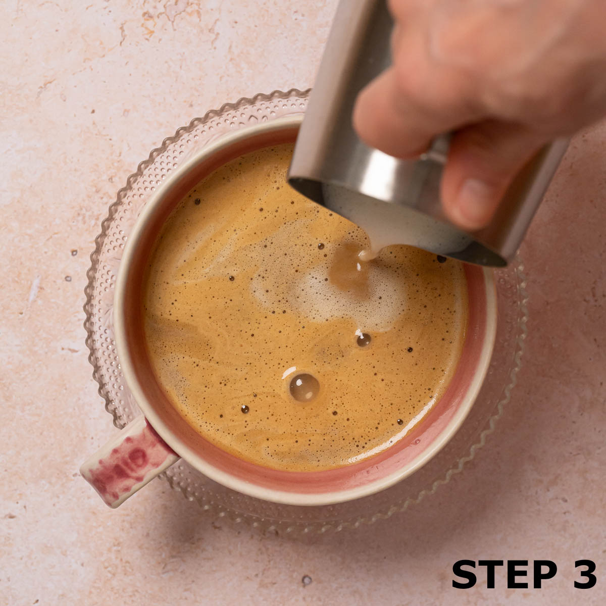 A person pouring steamed milk into a cinnamon bun latte.