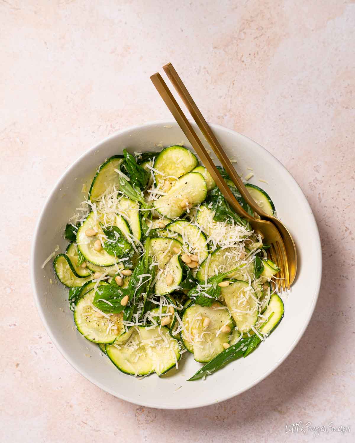 Raw courgette salad with basil, parmesan and pine nuts in a bowl with gold cutlery.