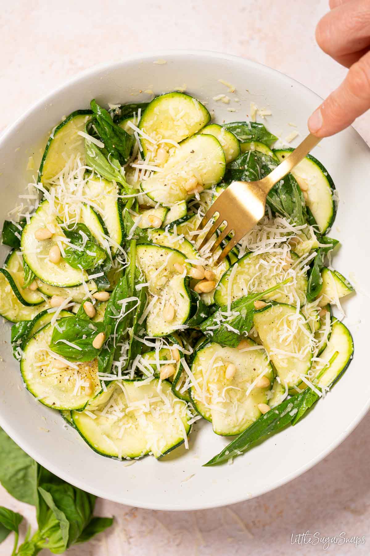 Basil salad with courgette, parmesan and pine nuts with a fork in the bowl.