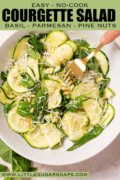 Labelled salad with courgette, basil, parmesan and pine nuts with a fork in the bowl.