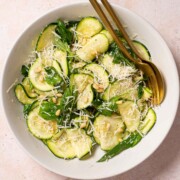 Raw courgette salad with basil, parmesan and pine nuts in a bowl with gold cutlery.