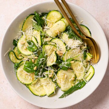 Raw courgette salad with basil, parmesan and pine nuts in a bowl with gold cutlery.