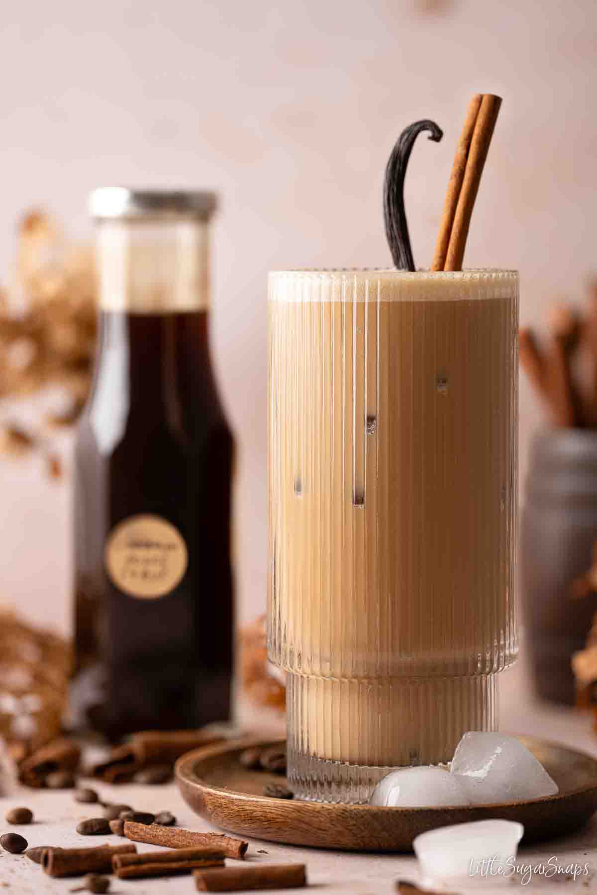 A glass of iced cinnamon latte with cinnamon stick & vanilla pod garnish.