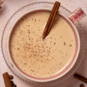 Cinnamon bun latte in a pink mug with cinnamon stick and ground spice garnish.
