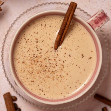 Cinnamon bun latte in a pink mug with cinnamon stick and ground spice garnish.