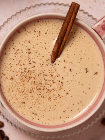 Cinnamon bun latte in a pink mug with cinnamon stick and ground spice garnish.