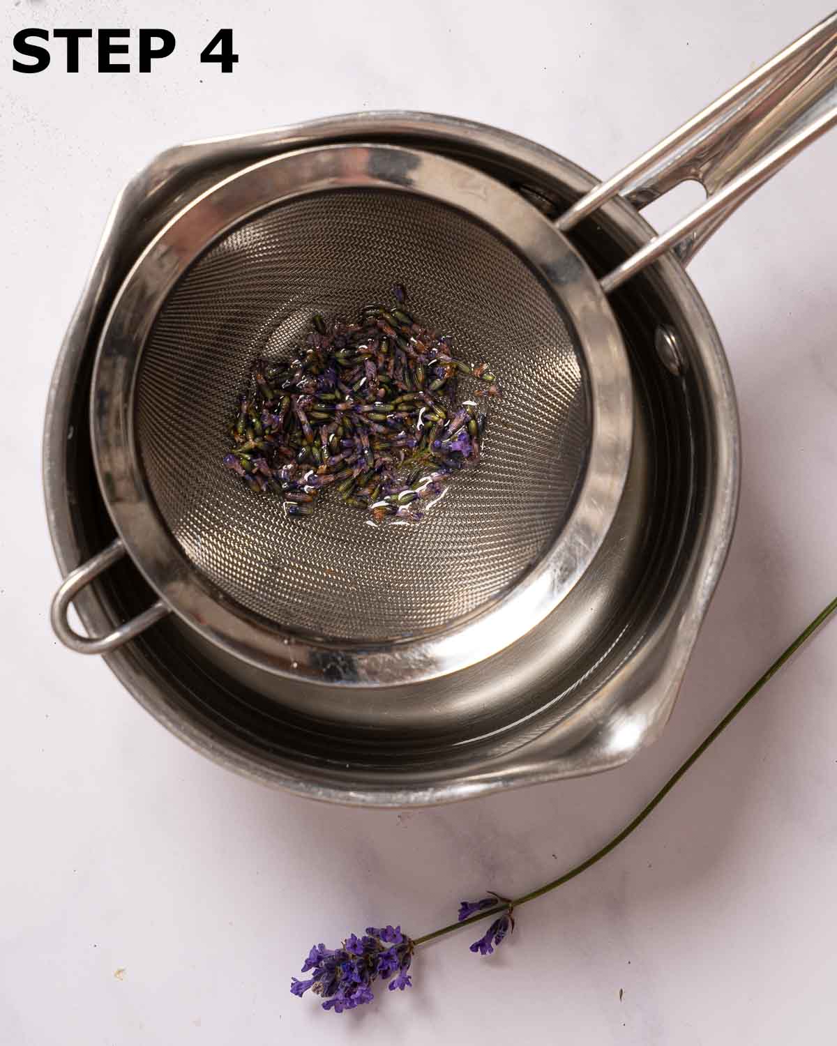 Lavender buds in a sieve suspended over a pan.