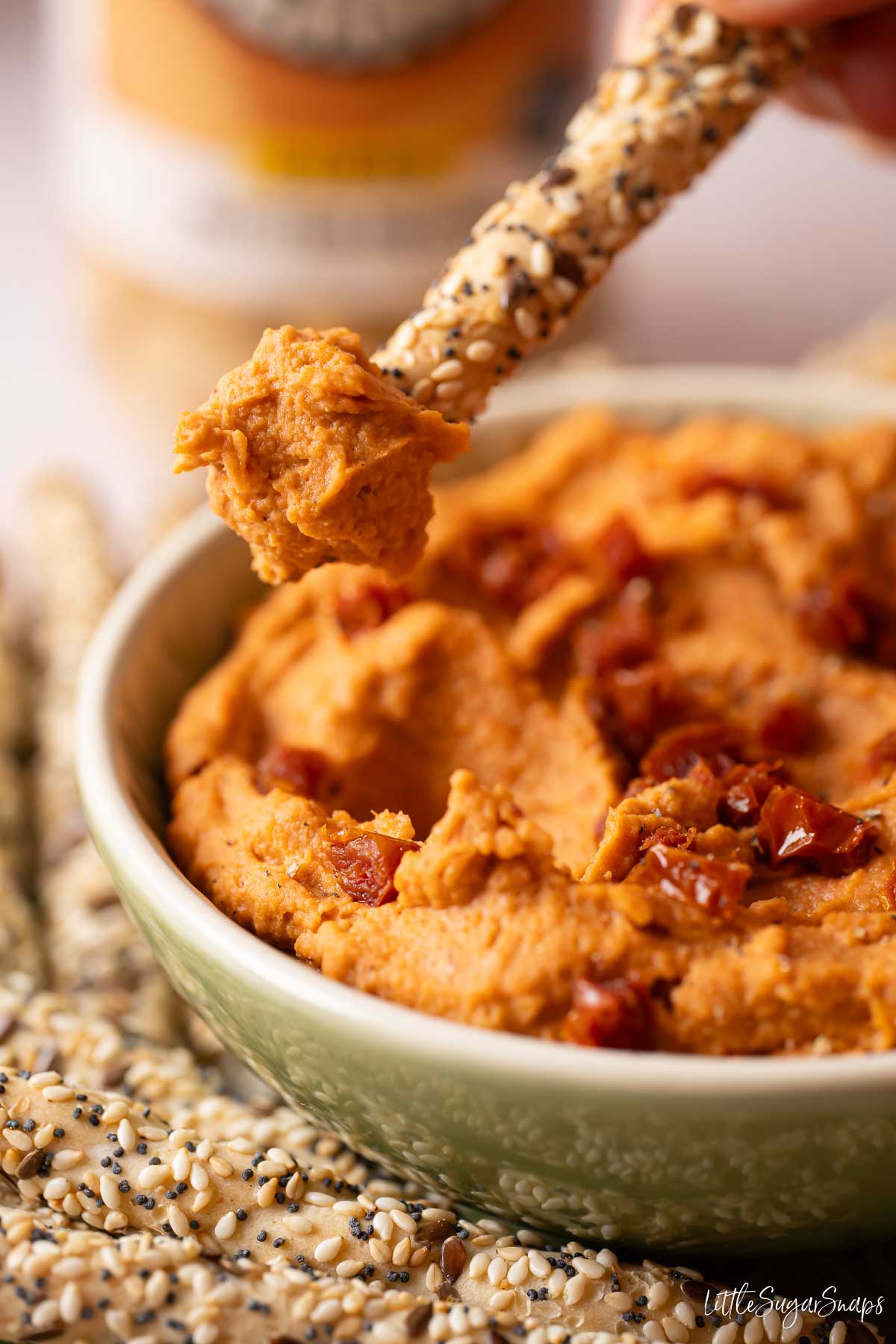 Sun-dried tomato and white bean dip scooped onto a seeded breadstick from a bowl.